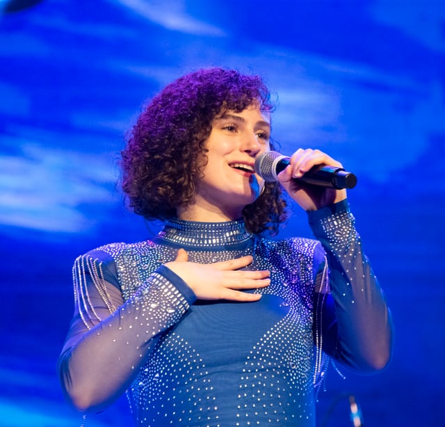 Grace Wright singing with her hand on her heart in a sparkling blue outfit