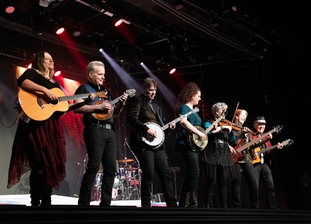 The Duttons playing guitars, banjo and fiddles across a smoky stage