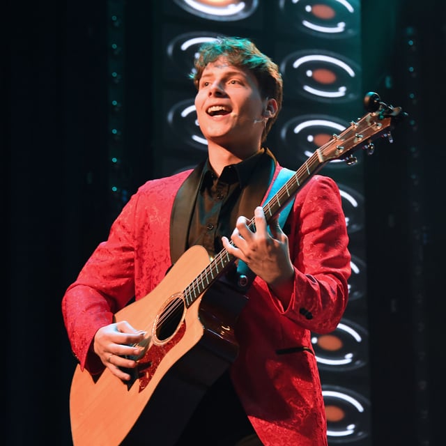 Tim Jr Dutton singing and playing acoustic guitar in a red sequin jacket