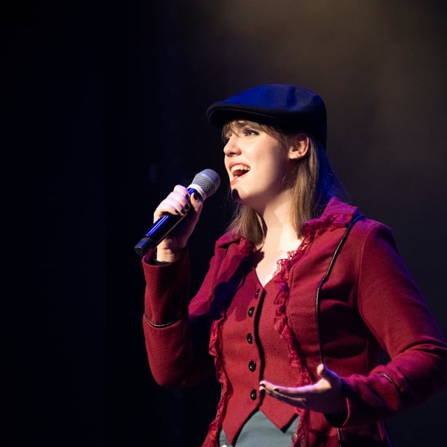 Elena Dutton singing in a red jacket and newsboy cap