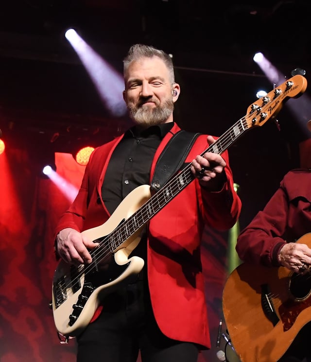 Steve Leach smiling as he plays bass guitar in a red jacket