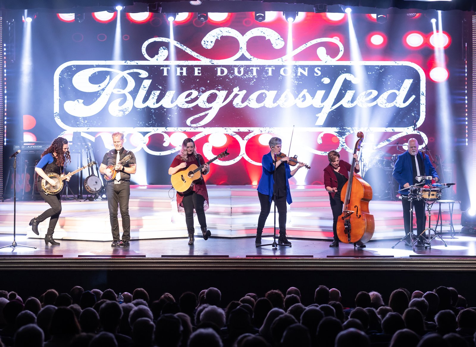 The Duttons playing banjo, guitars, fiddle and upright bass under a lighted “Bluegrassified” sign