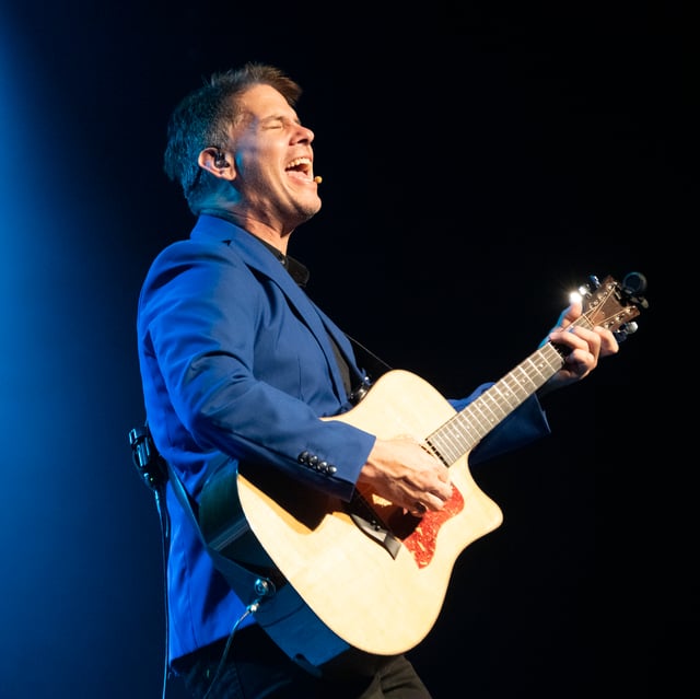 Jonathan Dutton singing and playing acoustic guitar in a blue jacket