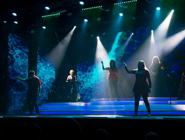 Performers on stage under bright blue and white spotlights