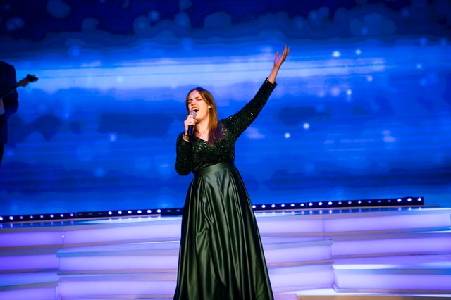 Elena Dutton singing with one arm raised in a green gown