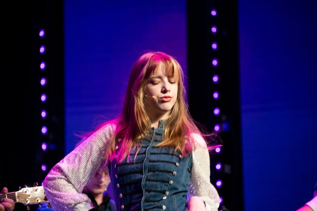 Lilah Dutton singing on stage in a denim vest