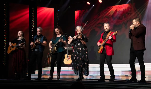 Six Duttons with fiddles, guitars and harmonica on a red-lit stage