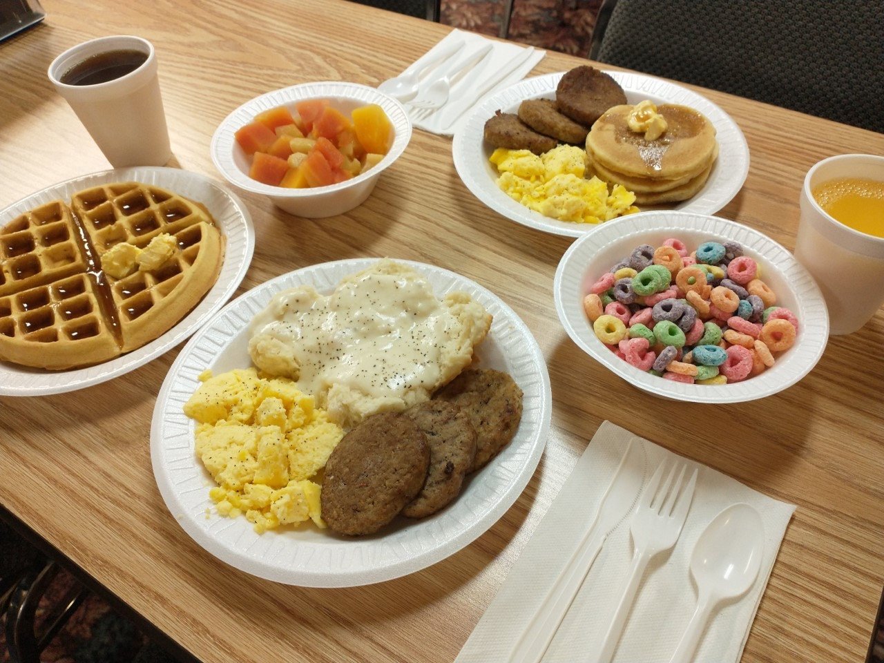 Breakfast plates of waffles, scrambled eggs, sausage, biscuits and gravy, pancakes, fruit and cereal