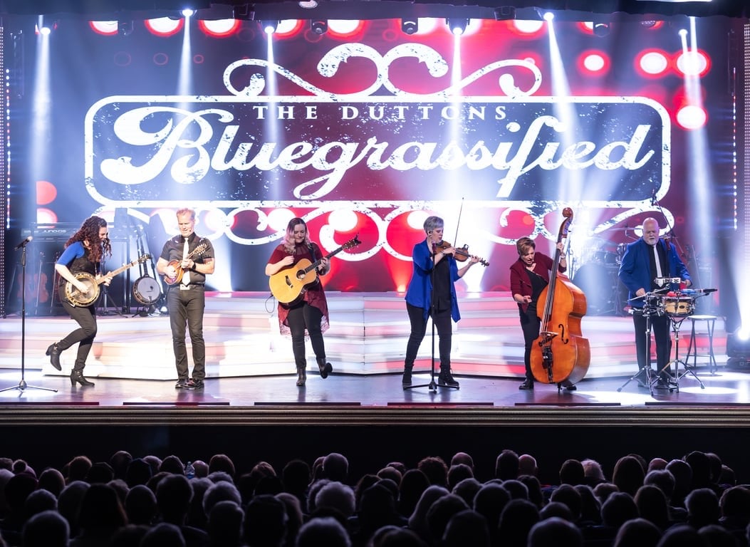 The Duttons playing banjo, fiddle and bass under a Bluegrassified sign
