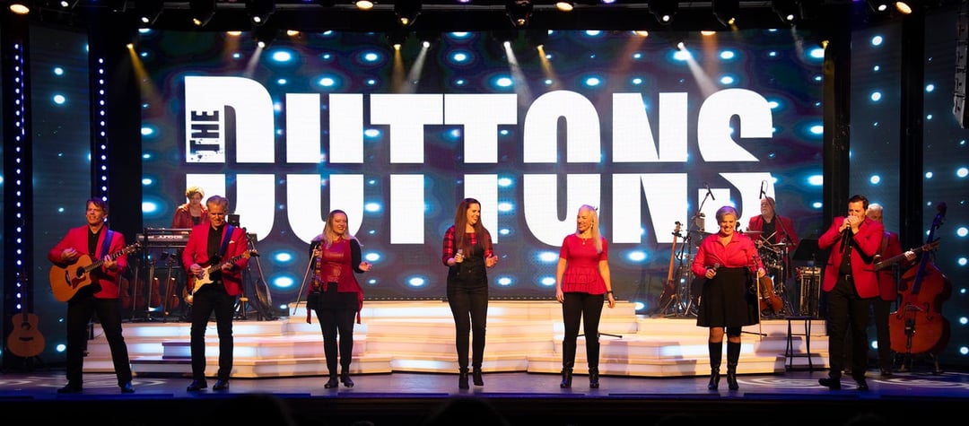 The Duttons in red, lined up across the stage under a lit-up DUTTONS sign