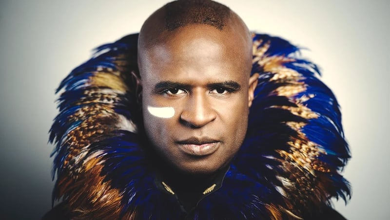 Alex Boyé in a dramatic feathered collar with white face paint