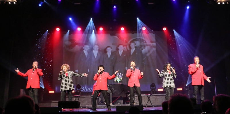 The Blackwoods and The Duttons singing together on stage under red and blue lights