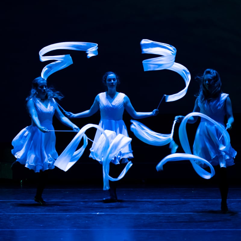 Celtic Throne dancers twirling white ribbons on a blue-lit stage