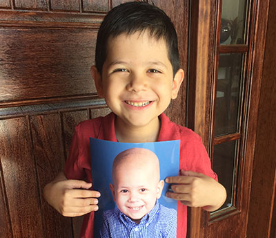 Josiah Dutton smiling and holding up a photo of himself during chemotherapy