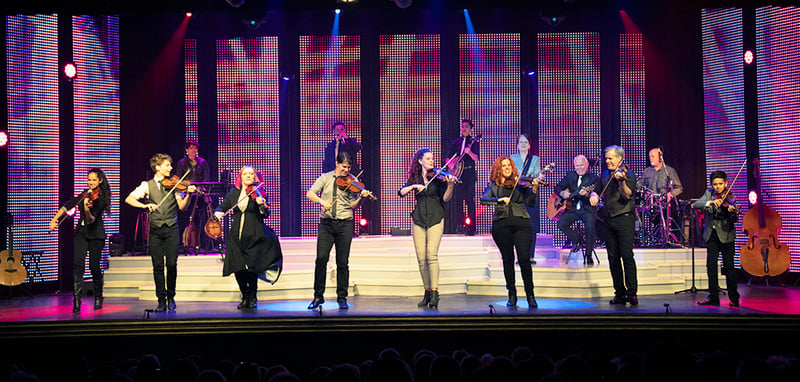 The Duttons in a line across the stage playing fiddles and guitars
