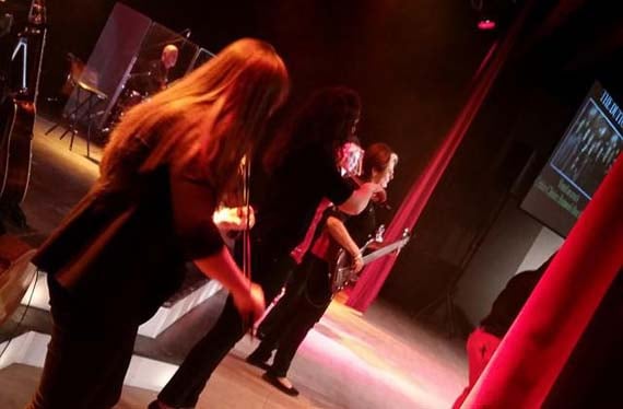 A Dutton performer playing fiddle on a red-lit stage