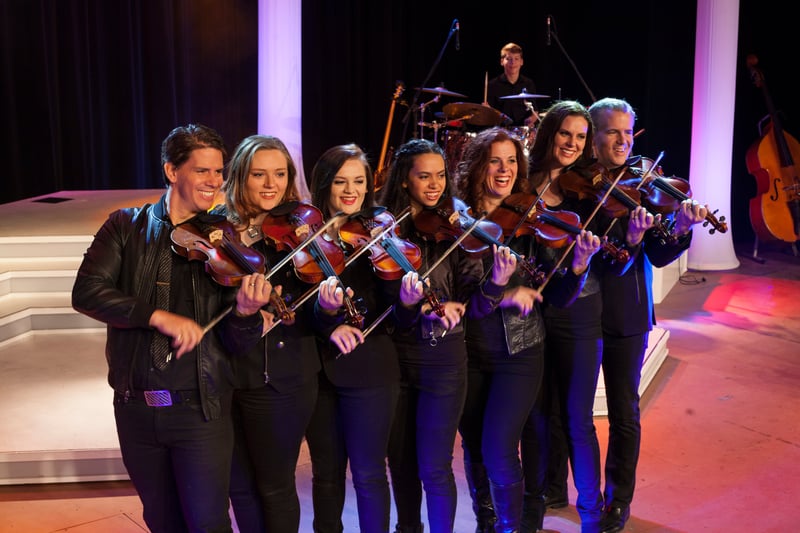Seven Duttons playing fiddles in a line across the stage