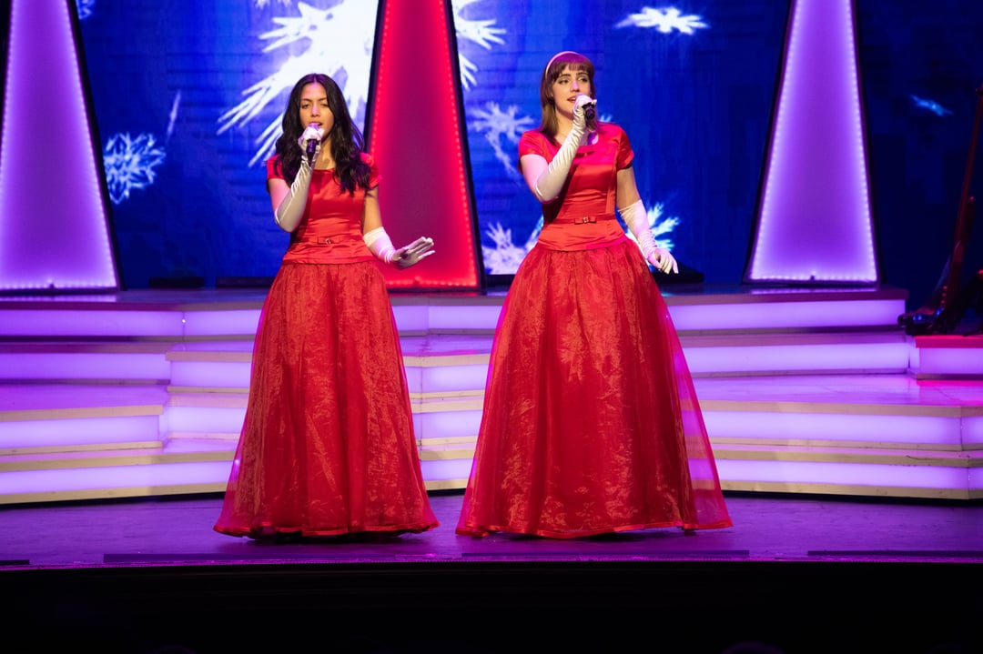 Two Dutton sisters in red ball gowns singing under snowflake lights