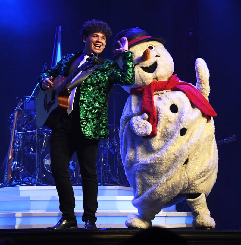 A guitarist in a green sequin jacket performing next to a dancing snowman