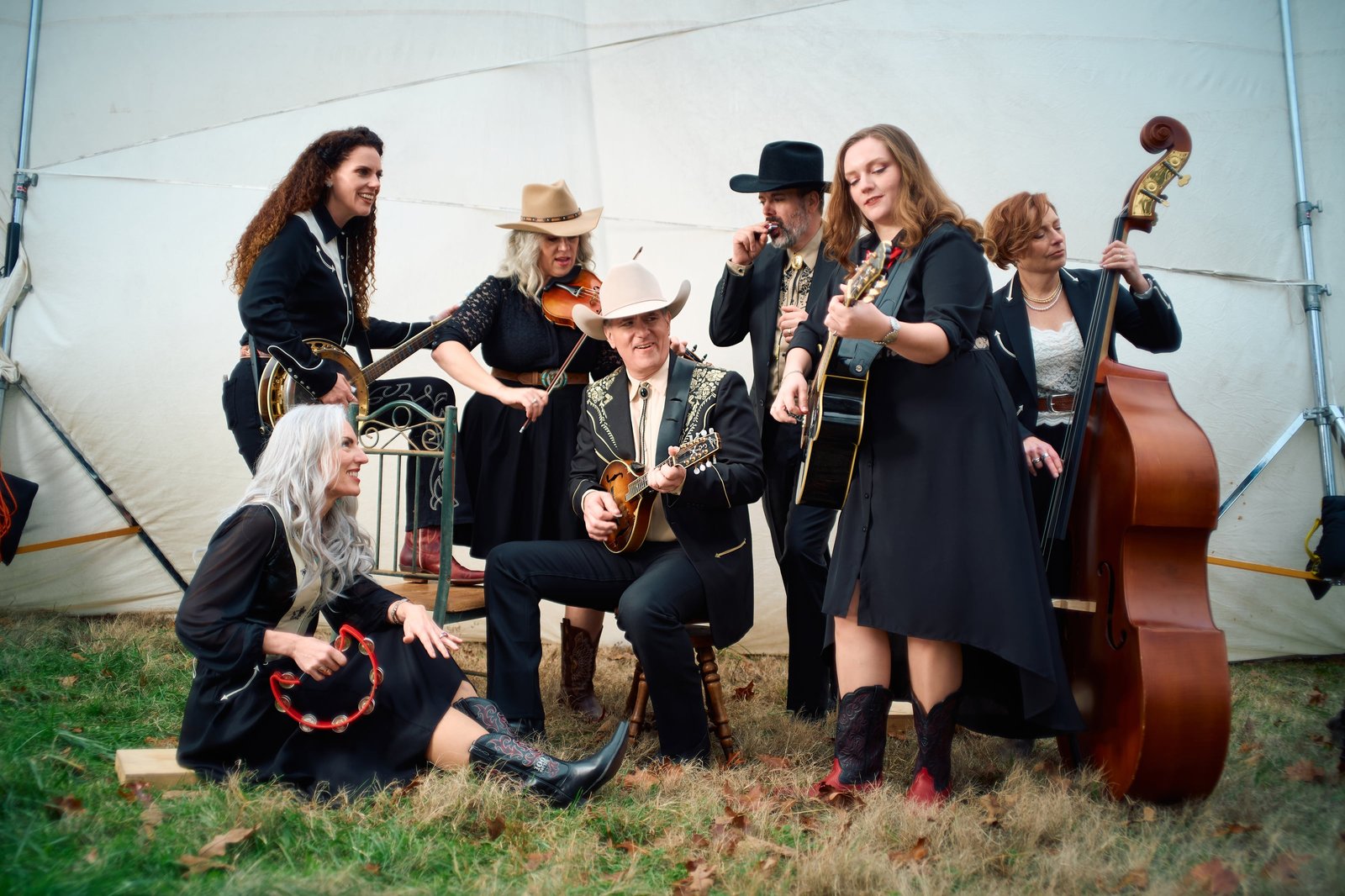 Seven Duttons with fiddles, guitars, banjo and upright bass posed in front of a white tent
