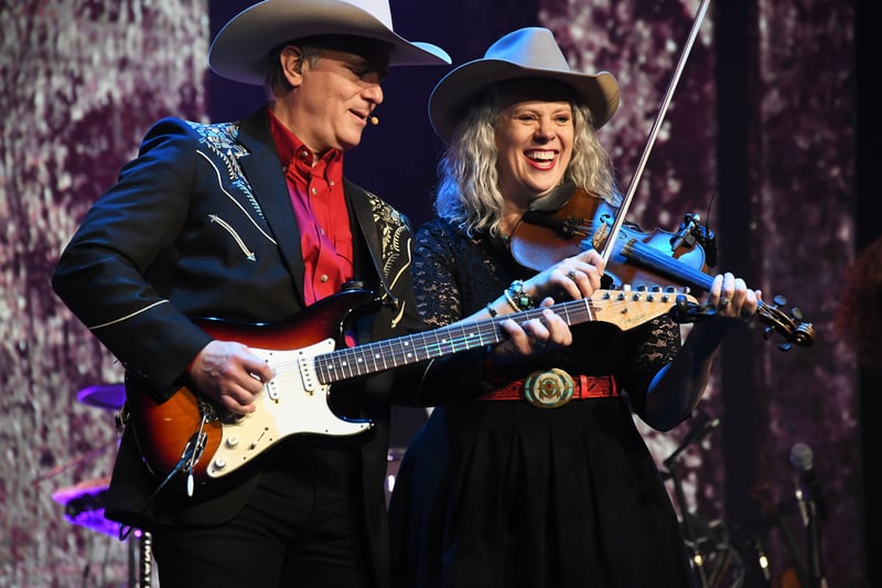 A guitarist and a smiling fiddler in cowboy hats playing side by side on stage