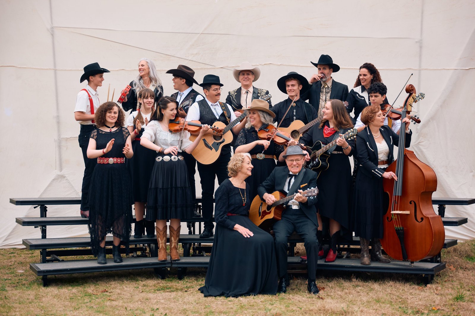 More than twenty members of the Dutton family, three generations, posing on risers with fiddles, guitars, banjos and an upright bass