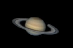 A blurry but distinct image of a pale yellow planet with oval rings around it.