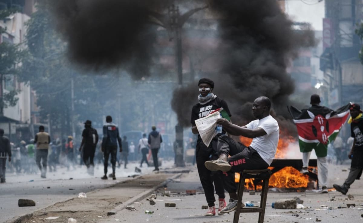 A protester holds a newpaper while smoke billows from a burning barricade during an anti-government demonstration