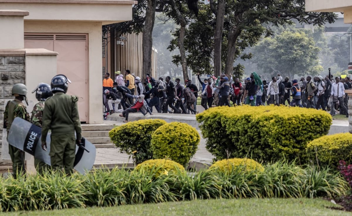 Protesters run inside the Kenyan Parliament as Kenya Police officer look at them on June 25