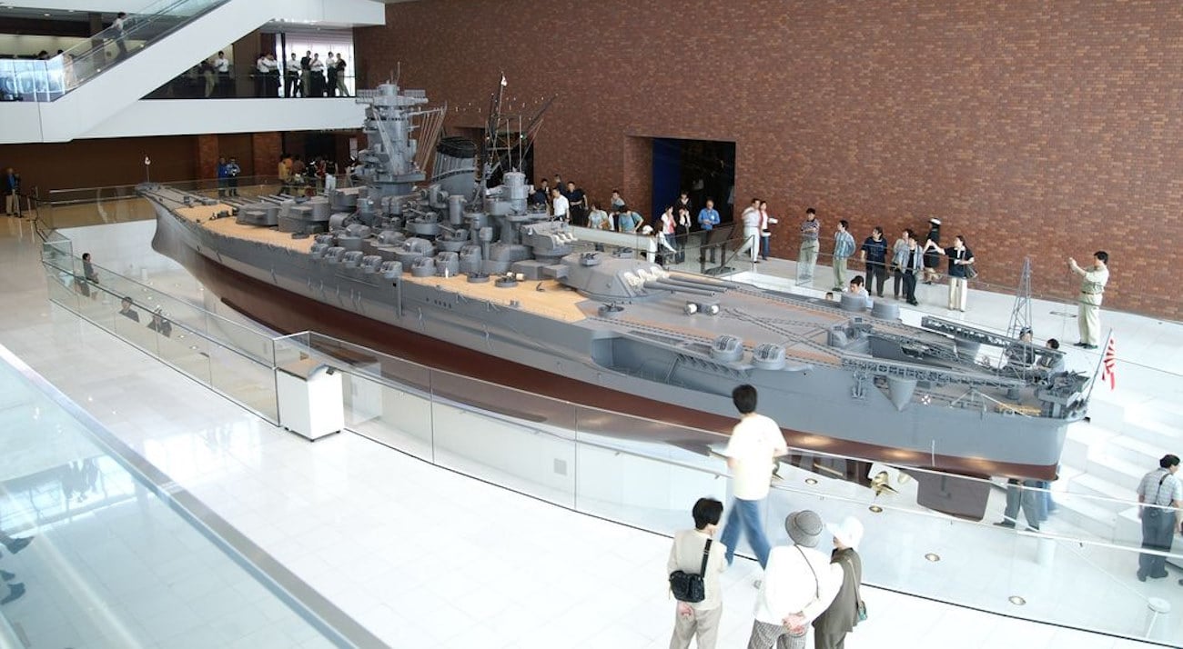 Vue d'ensemble d'une grande maquette du cuirassé Yamato au Musée maritime de Kure au Japon. Le modèle est très détaillé et présenté au centre d'une grande salle, entouré de visiteurs. L'architecture moderne du musée est visible en arrière-plan.
