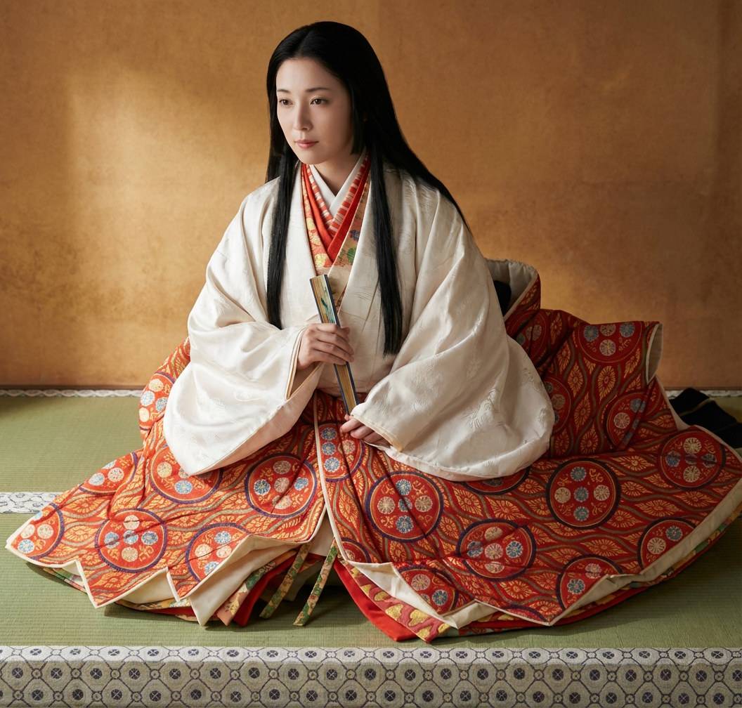 Oichi-no-kata en kimono traditionnel rouge et blanc avec éventail, assise en seiza sur tatami
