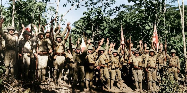 Soldats japonais célébrant la victoire après la chute de Bataan aux Philippines en 1942, levant les bras en signe de triomphe dans la jungle.