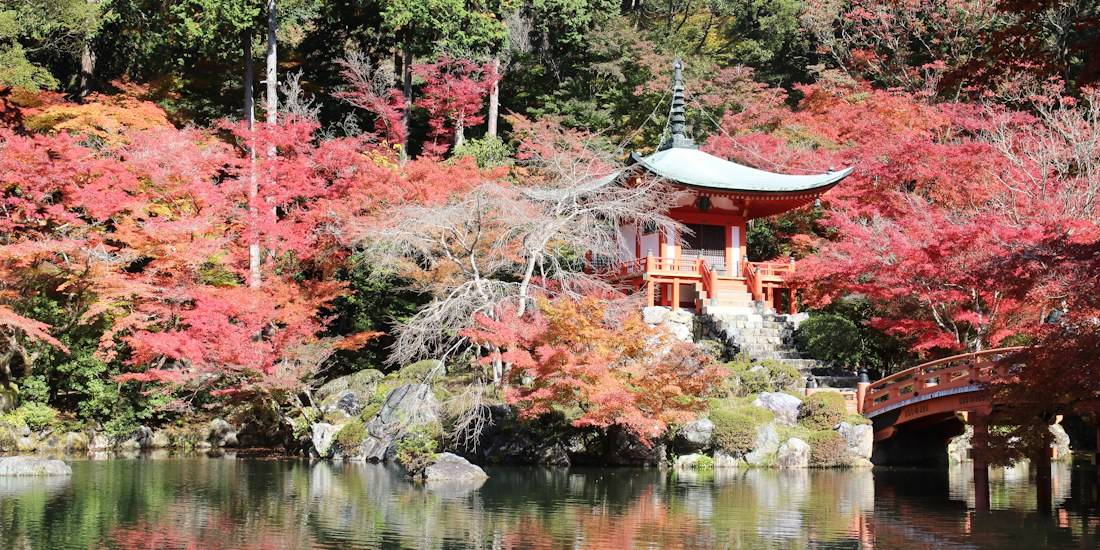 Temple Benten-do du complexe Daigo-ji à Kyoto entouré d'érables aux couleurs d'automne rouges et orangées se reflétant dans un étang avec un pont traditionnel en bois.