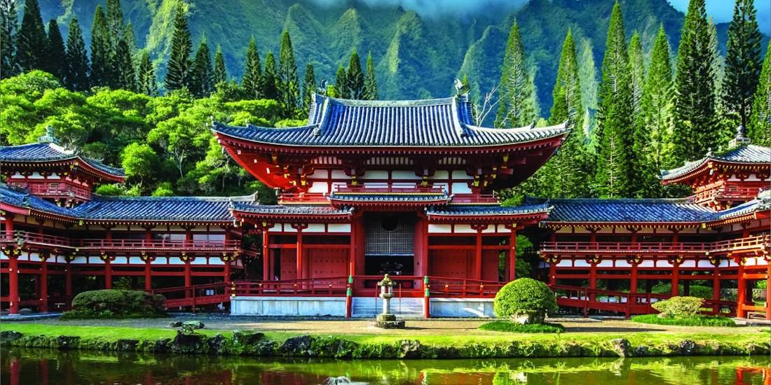 Temple Byodo-in à Uji près de Kyoto au Japon, architecture bouddhiste traditionnelle rouge avec toit bleu devant des montagnes verdoyantes et un étang.