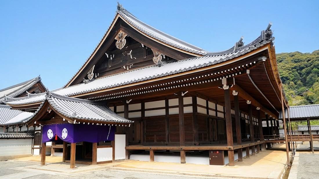 Temple Chion-in à Kyoto au Japon montrant l'architecture traditionnelle en bois du bâtiment Shuedo sous un ciel bleu clair avec une colline verdoyante en arrière-plan.