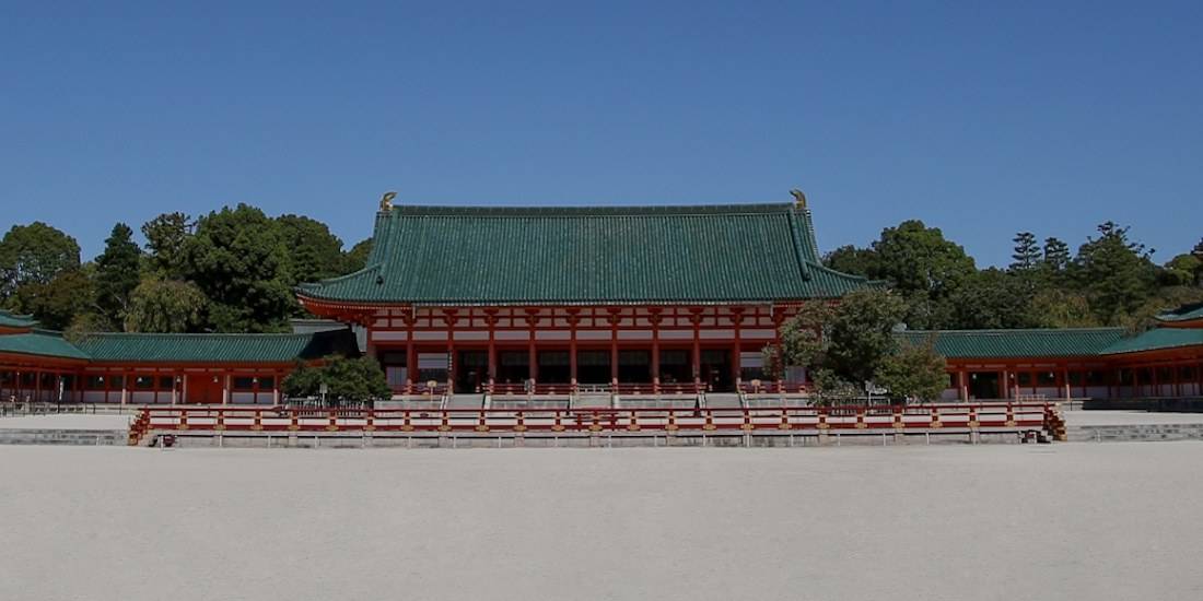 Vue panoramique du Daigoku-den, le bâtiment principal du sanctuaire Heian-jingu à Kyoto, avec son architecture impériale rouge et verte sous un ciel bleu.