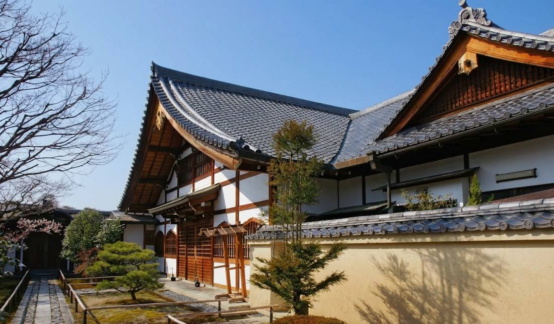 Temple Daitoku-ji à Kyoto avec son architecture traditionnelle en bois, ses toits de tuiles grises et un jardin zen sous un ciel bleu clair.