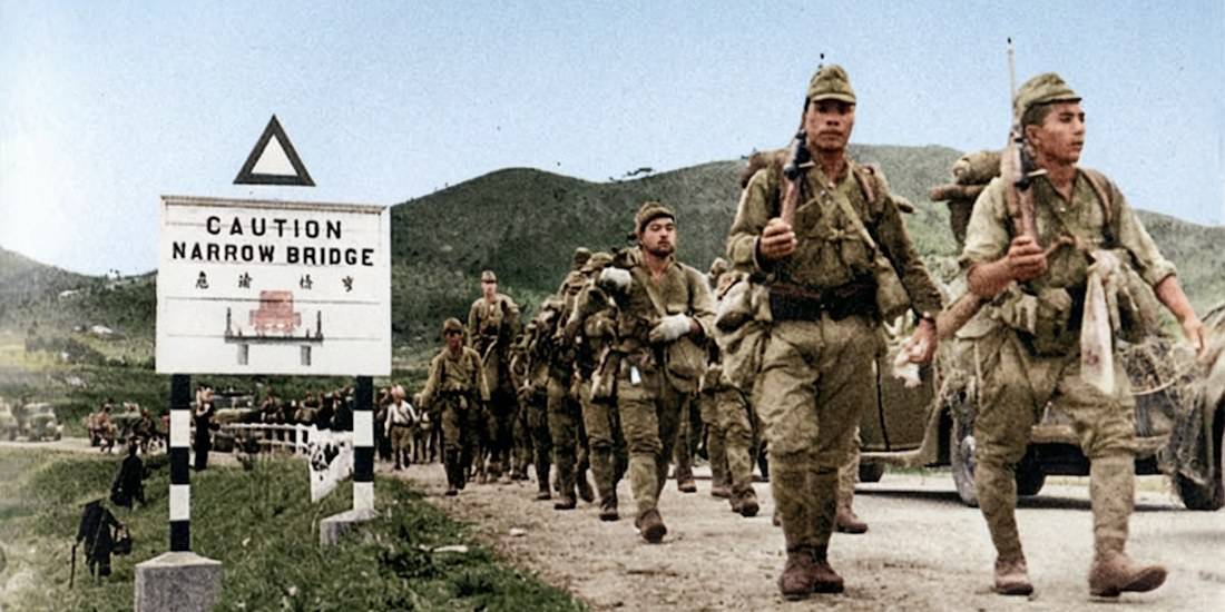 Soldats japonais du 228e régiment de la 38e division marchant devant un panneau de signalisation britannique lors de l'invasion de Hong Kong en décembre 1941.