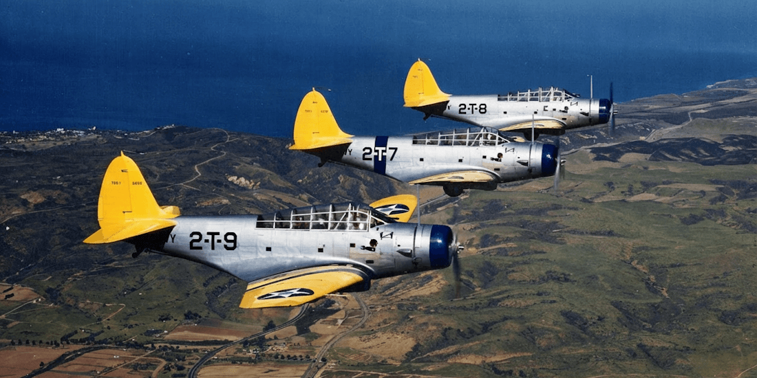 Trois avions bombardiers-torpilleurs Douglas TBD-1 Devastator de l'US Navy volant en formation au-dessus d'un paysage côtier.