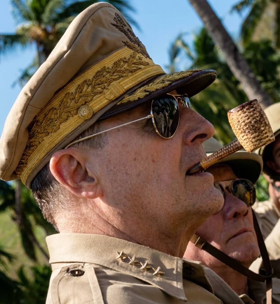 Portrait de profil du Général Douglas MacArthur portant sa casquette de commandement brodée d'or, ses lunettes de soleil aviateur emblématiques et fumant sa célèbre pipe en épi de maïs.