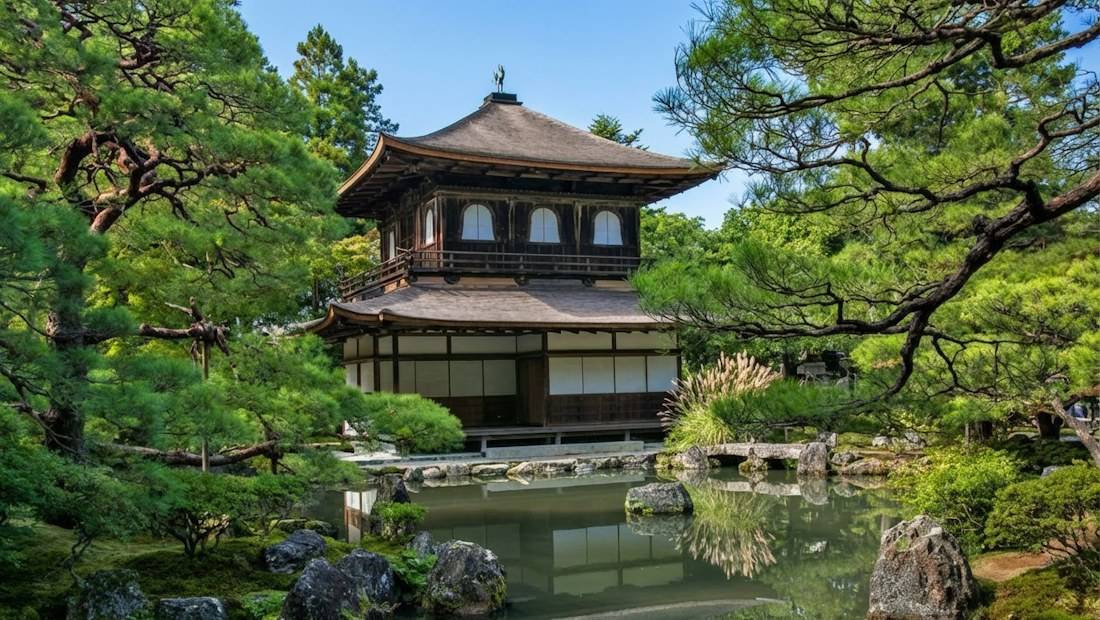 Vue du Ginkaku-ji, le Pavillon d'Argent à Kyoto, avec son architecture traditionnelle à deux étages se reflétant dans l'étang du jardin zen entouré de pins.