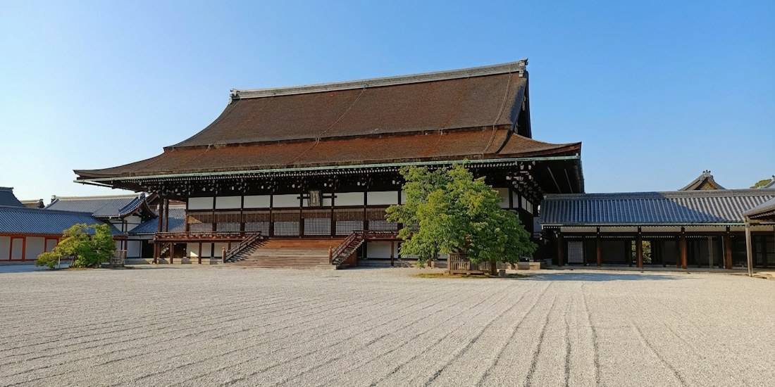 Vue d'ensemble du Shishinden, le hall de cérémonie principal du Palais Impérial de Kyoto (Kyoto Gosho), avec son architecture traditionnelle en bois et son jardin de gravier ratissé sous un ciel bleu.