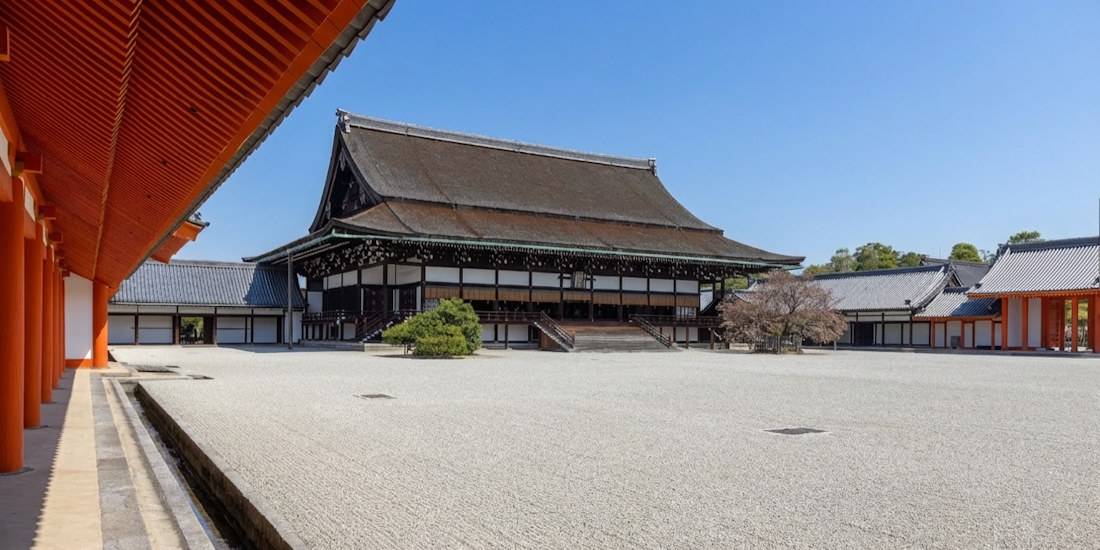 Vue panoramique du Shishinden, le bâtiment principal du Palais Impérial de Kyoto (Kyoto Gosho), avec son architecture traditionnelle japonaise, son toit en écorce de cyprès et sa cour de gravier blanc sous un ciel bleu.