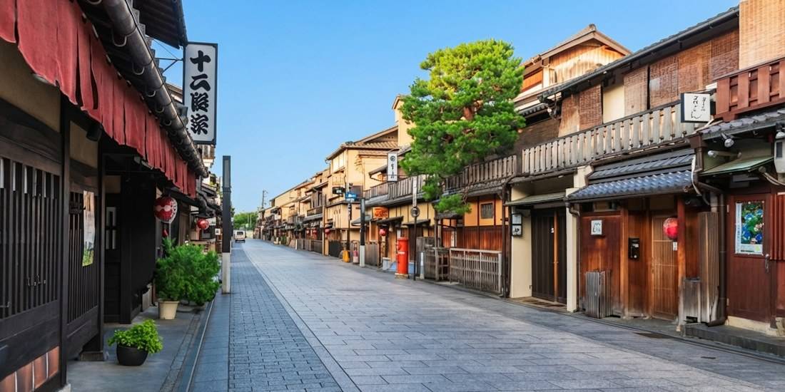 Rue pavée traditionnelle Hanamachi dans le quartier historique de Gion à Kyoto, Japon, bordée de maisons en bois machiya sous un ciel bleu clair.
