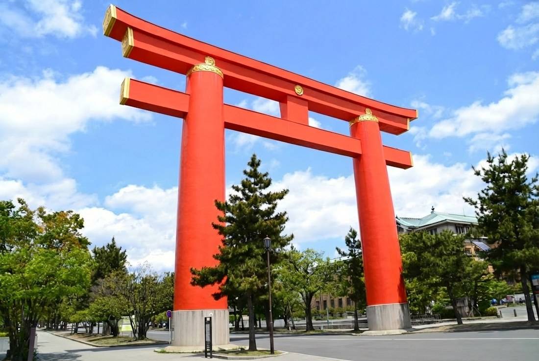 Grand torii rouge vermillon du sanctuaire Heian-jingu à Kyoto sous un ciel bleu avec des arbres verdoyants, monument emblématique du Japon.
