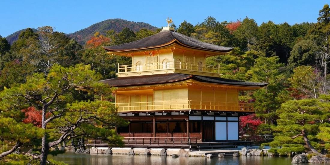 Temple du Pavillon d'Or Kinkaku-ji à Kyoto au Japon entouré d'arbres et reflété sur l'étang sous un ciel bleu.