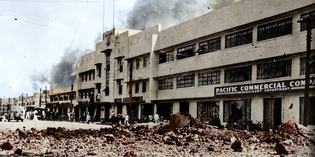 Destruction de bâtiments à Manille, Philippines, en 1941 après un bombardement, montrant des décombres au premier plan et de la fumée s'élevant des immeubles de la Pacific Commercial Company.