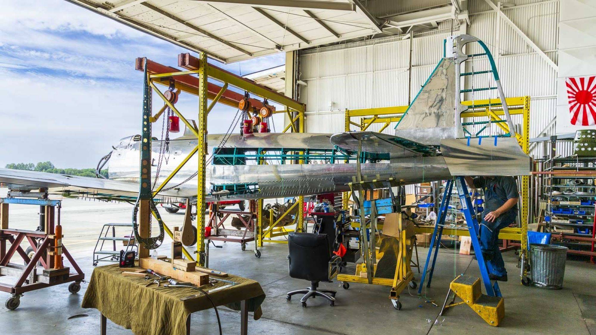 Restauration d'un avion de chasse japonais Mitsubishi A6M3 modèle 32 Zero dans le hangar du Military Aviation Museum, montrant la structure métallique et le fuselage en cours de reconstruction.