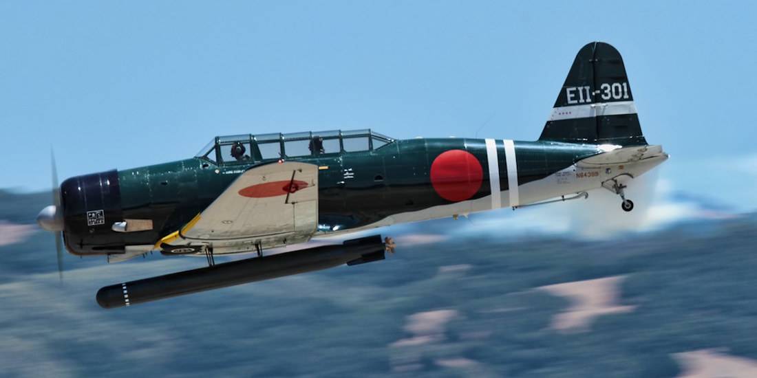 Avion bombardier-torpilleur japonais Nakajima B5N2 Kate en vol transportant une torpille, avec cocardes Hinomaru et marquages de queue EII-301 sur fond de paysage flou.
