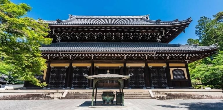emple bouddhiste Nanzen-ji à Kyoto avec son architecture traditionnelle en bois, son brûleur d'encens au premier plan et une végétation luxuriante sous un ciel bleu.